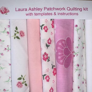 May include: A Laura Ashley patchwork quilting kit with templates and instructions, featuring eight folded fabric strips in various shades of pink and white, decorated with floral patterns, rose motifs, and a large stylised petal design.