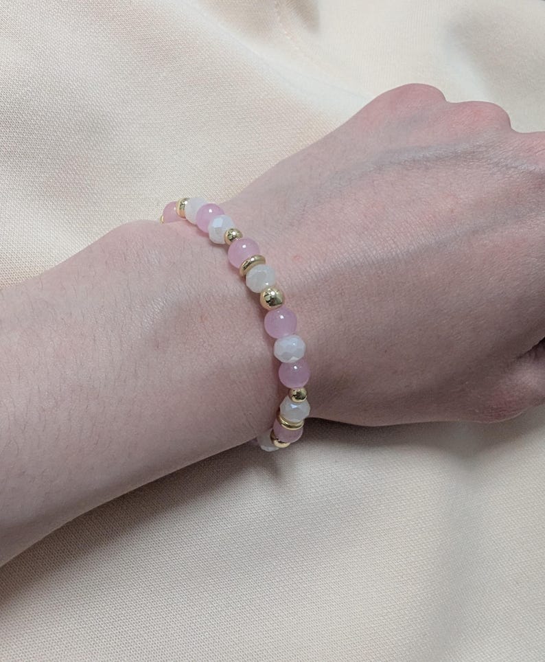 Puede incluir: Una pulsera de cuentas que presenta una alternancia de cuentas redondas rosas, cuentas blancas transl&uacute;cidas y peque&ntilde;as cuentas espaciadoras met&aacute;licas de tono dorado. La pulsera est&aacute; hecha con un cord&oacute;n el&aacute;stico flexible.