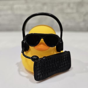 May include: A yellow rubber duck wearing black sunglasses, a headset, and holding a black keyboard. The keyboard has the word "Sweet" on it. The duck has an orange beak and is set against a neutral background.