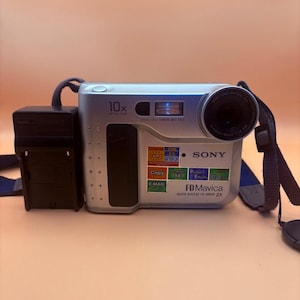 May include: Silver Sony FD Mavica digital camera with a black lens and strap. Features include 10x optical zoom, copy, and email functions. Includes a black battery pack. The camera has the text "FD Mavica QUICK ACCESS FD DRIVE 2X".