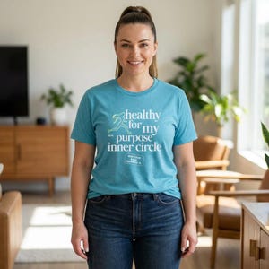 May include: A teal t-shirt with the text "healthy for my purpose inner circle" in white. The shirt also features a graphic of a person running. The text "Run Tour Orlando, FL" is also printed on the shirt. The person is wearing blue jeans.