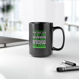 May include: Black coffee mug with a white rim and handle. The mug has green text that reads "The Original Diet", "Then God Said I Give You Every Seed-Bearing Plant on the Face of the Whole Earth and Every Tree That Has Fruit With Seed in It. They Will Be Yours For Food. Genesis 1:29".