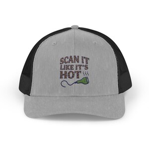 Peut inclure: Casquette de camionneur grise avec un dos en filet noir. Le devant de la casquette porte le texte brodé "SCAN IT LIKE IT'S HOT" au-dessus d'un graphique vert et bleu d'un scanner médical.