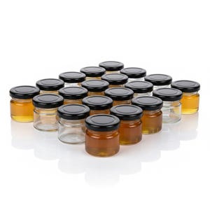 May include: A collection of twenty small, clear glass jars arranged in a grid. Each jar features a round, black metal screw-top lid. Some of the jars are filled with a golden-amber liquid, while others are empty, showing the transparent glass.