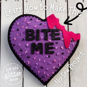 May include: Purple felt heart with black felt trim and the words "Bite Me" in black glitter. The heart has a bite taken out of it, revealing pink felt underneath. The words "No Sew Project" are written in white on a black background in the bottom right corner.
