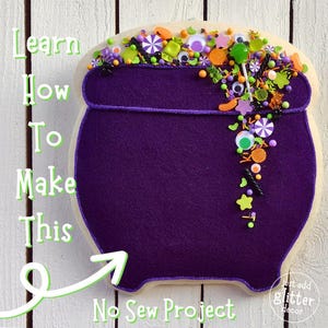 May include: A purple cauldron cookie decorated with sprinkles, candy eyes, and a lollipop. The cookie is on a white wood background with the text "Learn How To Make This No Sew Project" written in green.