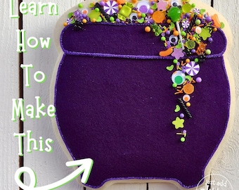 Puede incluir: Una galleta de caldero morado decorada con chispas, ojos de caramelo y una piruleta. La galleta está sobre un fondo de madera blanca con el texto "Learn How To Make This No Sew Project" escrito en verde.