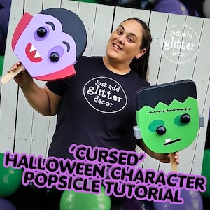 May include: Two handheld Halloween character decorations on wooden sticks. One is a purple vampire with black hair, red accents, and white fangs. The other is a green Frankenstein monster with black hair, stitches, and a single white tooth.