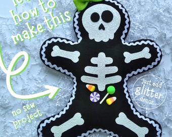 Puede incluir: Una figura de esqueleto de fieltro negro estilo hombre de jengibre con cráneo, caja torácica y huesos de purpurina plateada. Incluye un lazo verde lima, adornos de caramelos y ribete en zigzag blanco. Texto: learn how to make this, no sew project, just add glitter decor.
