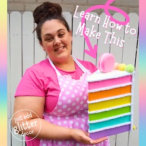May include: A woman in a pink polka dot apron holds a large rainbow layered cake. The cake is decorated with white frosting, sprinkles, and a pink macaron. The text "Learn How to Make This" is written in pink above the cake.
