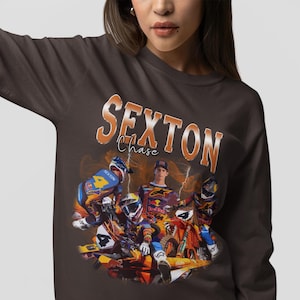 Puede incluir: Una camiseta de manga larga marrón con un gráfico de estilo vintage de un piloto de motocross. El gráfico presenta el texto "SEXTON Chase" en naranja y amarillo.