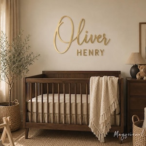 May include: A dark wood cot with a beige mattress and a cream-coloured fringed throw blanket. Mounted on the wall above the cot is a gold-coloured sign featuring the name Oliver in a cursive script font and the name HENRY in a block font.