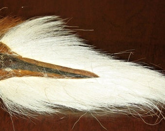 Può includere: Un oggetto decorativo naturale, con una combinazione di pelliccia bianca, marrone e nera. La pelliccia è lunga e fluente, con una sezione centrale scura. Sembra una coda di animale o un accessorio simile.