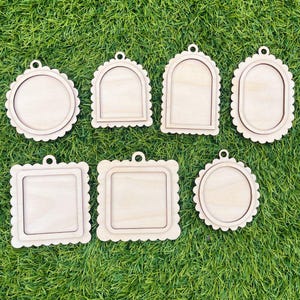 May include: A set of seven light-colored wooden ornaments with scalloped edges, featuring various shapes including circles, squares, arches, and ovals. Each piece has a small hole at the top for hanging and a recessed center area.