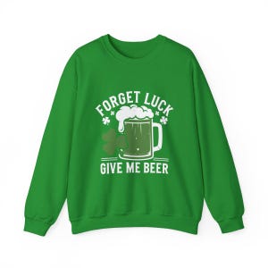 May include: Green sweatshirt with the text "FORGET LUCK GIVE ME BEER" in white. The design includes a beer mug with foam, shamrocks, and stars. A festive St. Patrick's Day themed apparel item.