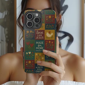 May include: A colorful phone case with a patchwork design featuring floral and heart motifs, and the phrases "love like Jesus" and "Made for More." The case has a dark background and a variety of colors.