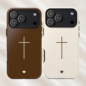 May include: Two phone cases, one brown and one cream, each featuring a cross design. The brown case has a white cross and a white heart, while the cream case has a brown cross and a brown heart. Both cases have a black camera module.