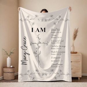 May include: Cream-colored blanket with black text and floral accents. The blanket features a cross design and the words "I AM" followed by inspirational phrases and Bible verses. The name "Mary Grace" is written on the side.