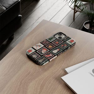 May include: A smartphone case featuring a festive Christmas-themed design. The case is covered in a grid of postage stamp-like squares, each displaying a different holiday image, including a snowman, Santa Claus, and a Christmas tree. The case is resting on a light-colored wooden surface.