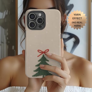 May include: A beige phone case featuring a Christmas tree design with a red bow and green tree. The case has a textured appearance with small white dots. The text "YARN EFFECT (NO REAL YARN)" is displayed on the image.