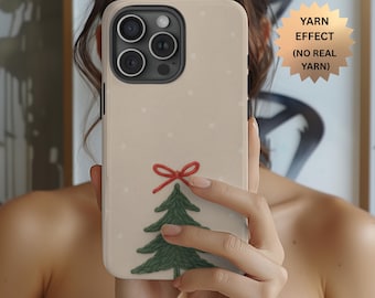 Puede incluir: Una funda de smartphone beige con un gráfico impreso de un árbol de Navidad verde coronado con un lazo rojo y pequeños puntos blancos. Una insignia dorada en forma de estrella contiene el texto YARN EFFECT (NO REAL YARN).