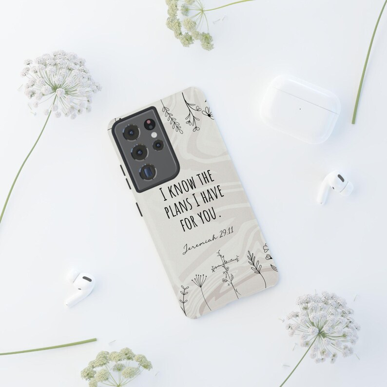May include: A white phone case with a beige marble pattern and black floral accents. The case features the text "I know the plans I have for you." with the scripture reference "Jeremiah 29:11".