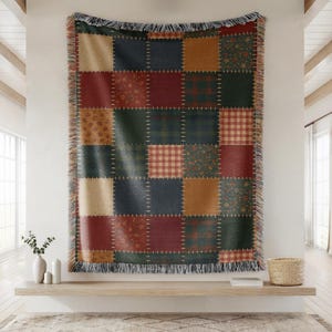 May include: A patchwork throw blanket with a variety of patterned squares in shades of red, green, tan, and navy blue. The blanket has a fringed edge and is displayed on a wall. The throw is approximately 60 inches wide and 70 inches long.