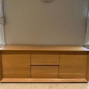 Puede incluir: Un armario de madera clara con dos puertas y un cajón. El armario tiene un diseño simple y moderno y está hecho de madera maciza.