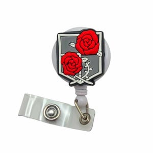 May include: A retractable badge reel with a white body and a clear plastic strap. The reel features a grey emblem with two red roses and a black outline. The badge reel is designed to hold an ID or access card.