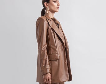 Könnte beinhalten: Braunes Kunstleder-Outfit, bestehend aus Blazer, Oberteil, Culottes und Plateau-Stiefeln. Der Blazer hat ein klassisches Design mit Taschen. Die Stiefel haben einen klobigen Absatz. Das Outfit ist einfarbig.