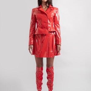 May include: A woman wearing a red patent leather jacket, skirt, and boots. She is wearing a red bucket hat.