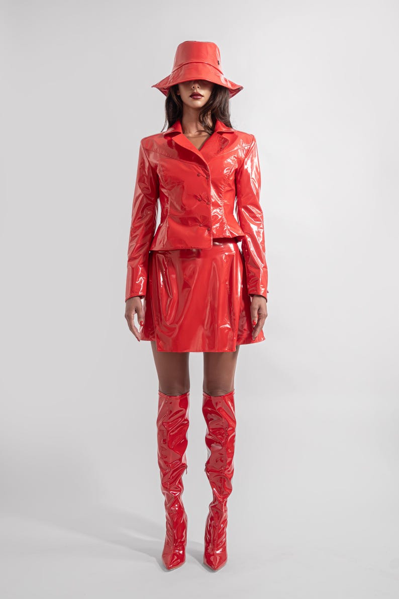 May include: A woman wearing a red patent leather jacket, skirt, and boots. She is wearing a red bucket hat.