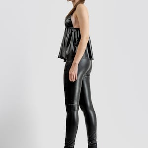 May include: A woman in a black halter top, leggings, and ankle boots. The boots have a gold decorative heel. The outfit is made of a shiny, leather-like material. The background is plain white.