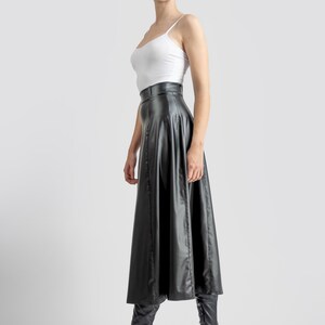 May include: A woman wearing a white tank top and a black leather midi skirt. She is wearing black knee-high boots with chunky heels.