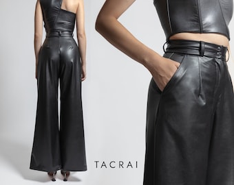 May include: A black leather pantsuit with a wide-leg silhouette and a one-shoulder top. The trousers have a high waist and a belt.