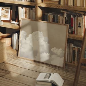 May include: A framed print of a cloudy sky with a light brown wooden frame. The print is leaning against a wooden bookshelf filled with books.