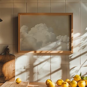 May include: A framed print of a cloudy sky with a wooden frame. A wooden cutting board and a group of lemons are on a countertop in front of the print.