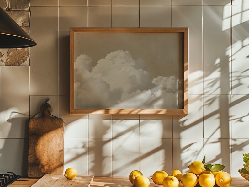 May include: A framed print of a cloudy sky with a wooden frame. A wooden cutting board and a group of lemons are on a countertop in front of the print.