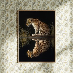 May include: A framed print of a leopard sitting by a body of water, with its reflection visible in the water. The leopard is brown and black with spots. The background is black.