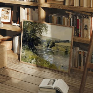 Pu&ograve; includere: Un dipinto incorniciato di una scena fluviale con alberi verdi e un cielo blu. Il dipinto &egrave; appeso a una libreria in legno con altri libri.