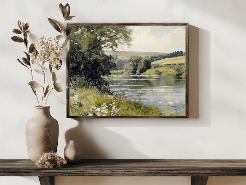 Pu&ograve; includere: Un dipinto incorniciato che rappresenta una scena fluviale con alberi verdi e colline sullo sfondo. Il fiume &egrave; calmo e riflettente, con alcuni fiori bianchi che crescono sulle rive.