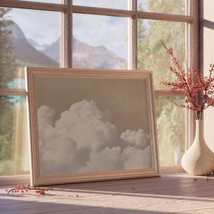 May include: A framed picture of a cloudy sky with a mountain range in the background, seen through a window. The picture is on a wooden surface with a vase of red berries and a small vase.