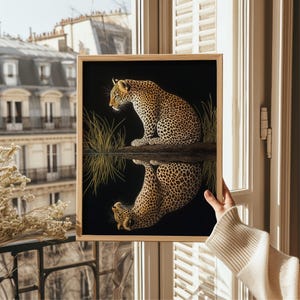 May include: A framed print of a black and white illustration of a leopard sitting in a grassy area. The leopard is looking to the left and its reflection is visible in the water below.