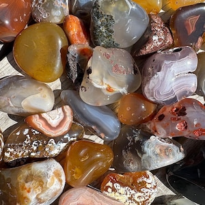 May include: A collection of agate stones in various shades of brown, white, and red. The stones are smooth and polished, with intricate patterns and swirls.
