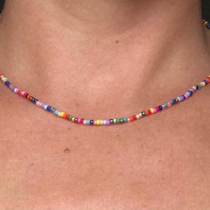 Puede incluir: Un collar de cuentas de colores con una variedad de cuentas pequeñas y redondas en tonos de rojo, naranja, amarillo, verde, azul, morado y rosa.