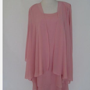 May include: A pink layered dress with a matching jacket. The dress has a scoop neckline and a flowing skirt. The jacket has long sleeves and a draped front.