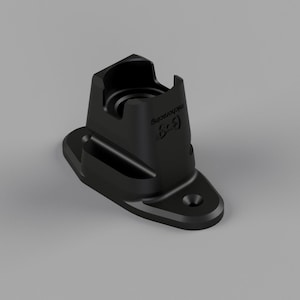 Puede incluir: Un objeto negro impreso en 3D con un cuerpo rectangular y una base redondeada. El objeto tiene una abertura cilíndrica en la parte superior y una pequeña ranura curva en el lateral. La base tiene un agujero para el montaje. El texto "5-3" es visible.