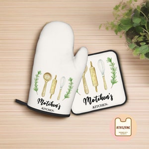 May include: White oven mitt and matching pot holder with black trim. Both feature a watercolour design of kitchen utensils and rosemary sprigs. The text "Motchen's Kitchen" is printed on both items.