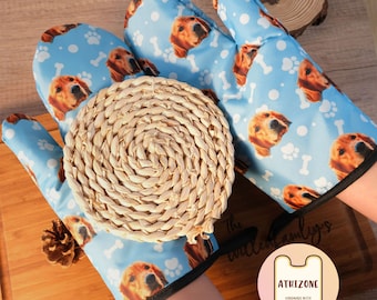 May include: A pair of blue oven mitts with a dog's face pattern. The mitts have a white background with paw prints and bone designs. The text "The Sweetest Family's" is visible in the background. The mitts are made by "Athizone Handmade with Enchanting".
