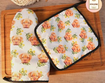 May include: A set of two white oven mitts with a black trim. The mitts feature a repeating pattern of a dog's face with yellow lemons and green leaves. The text "2024" is visible on the bottom right corner of the smaller mitt.